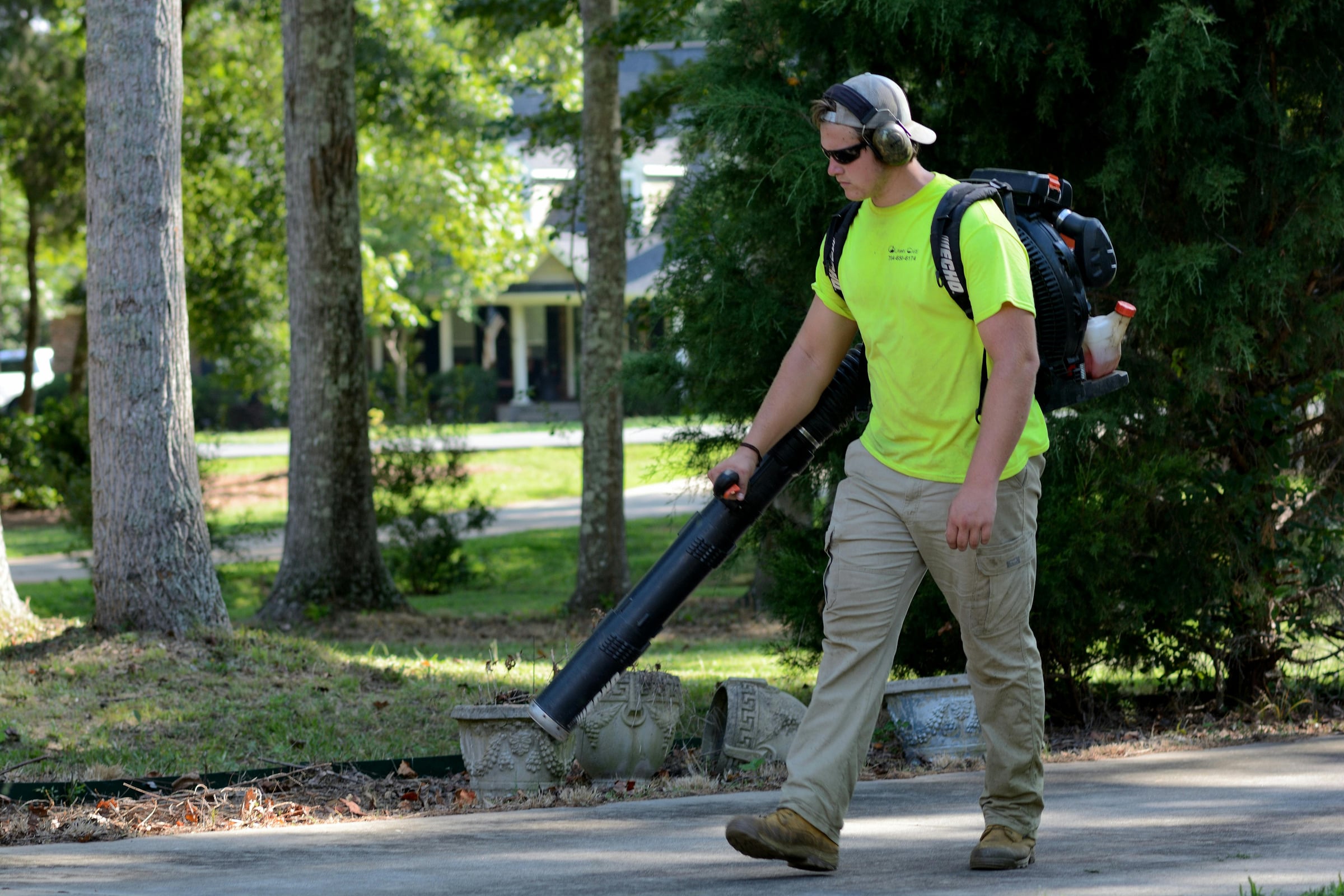 Worker using a backpack leaf blower to clear a driveway edge
